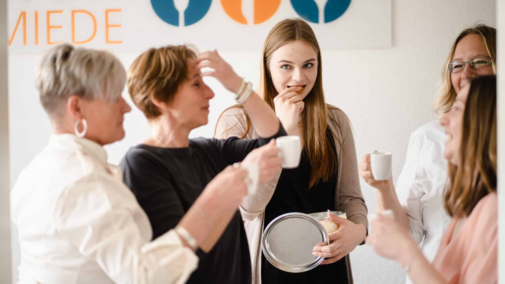 Fünf Frauen stehen zusammen und trinken Kaffee.